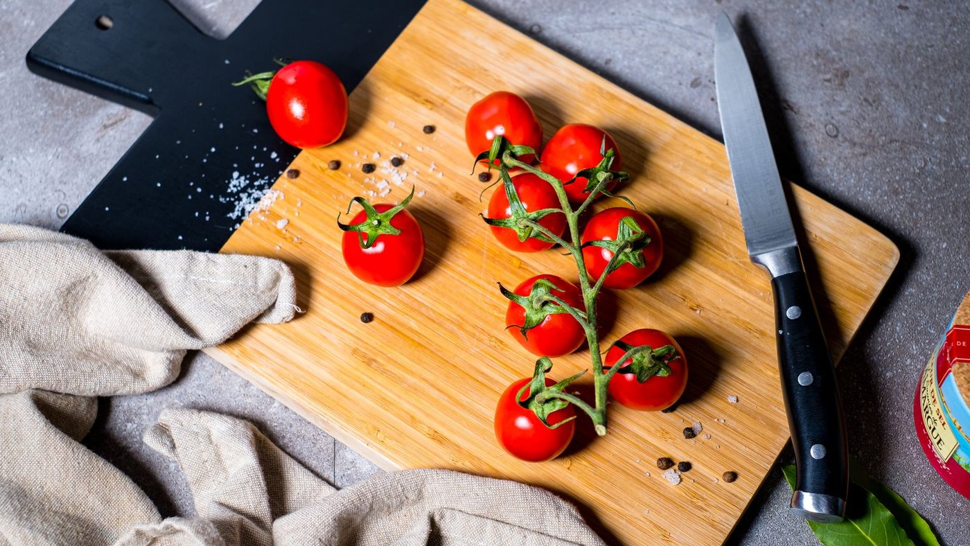 Томаты на светлой разделочной доске рядом с чёрной каменной