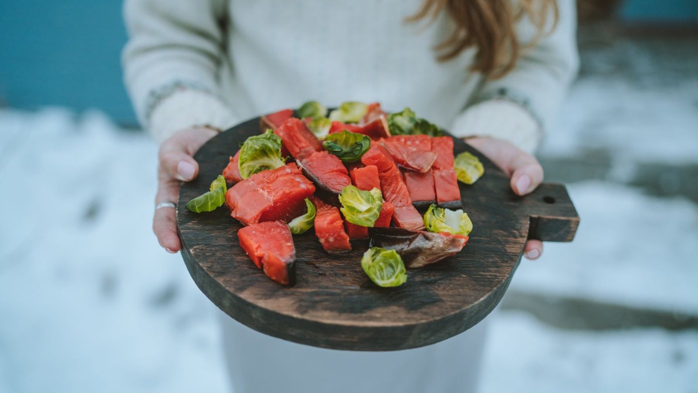 Деревянная доска с кусочками красной рыбы в руках зимой