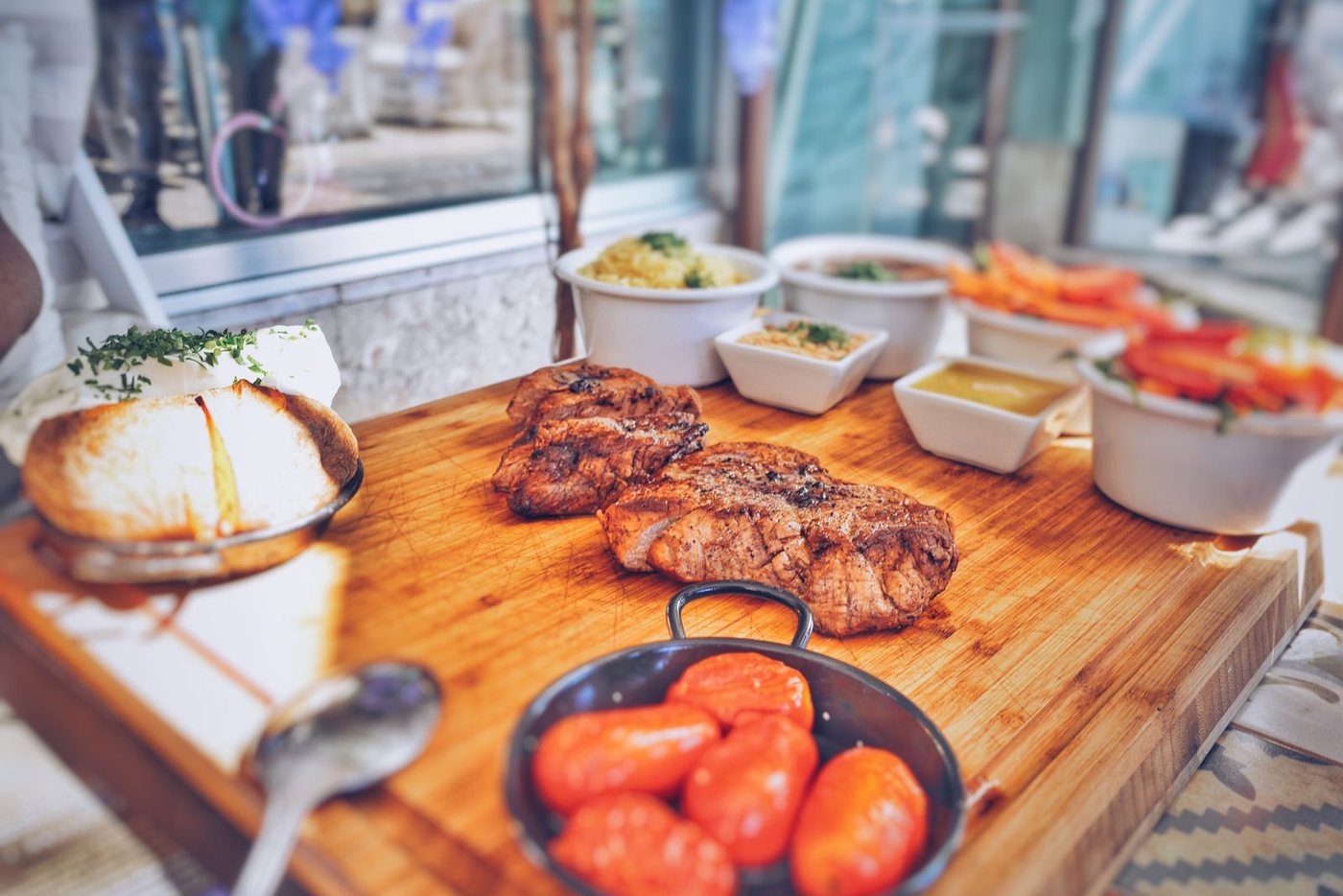 Жареное мясо на большой деревянной доске, гарниры и соусы в мисочках